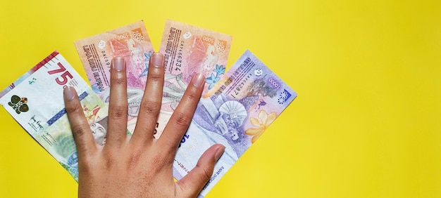 Mężczyzna trzyma nowe indonezyjskie banknoty na żółtym tle