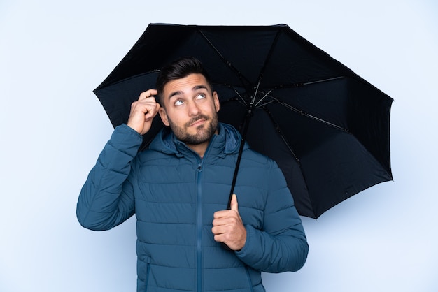 Mężczyzna trzyma parasol nad odosobnioną ścianą ma wątpliwości z zmieszanym twarzy wyrażeniem