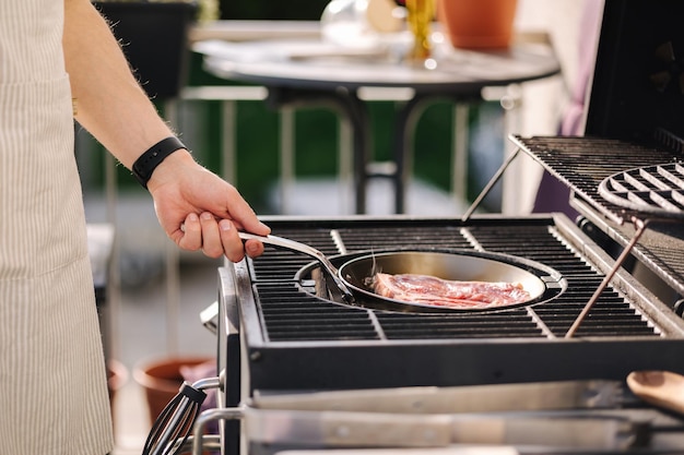 Mężczyzna trzyma patelnię na rozżarzonym węglu na grillu grillującym stek wołowy na widoku z boku patelni ze stali węglowej