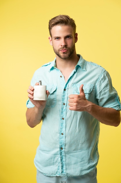Mężczyzna trzyma perfumy pokaz kciuk w górę mężczyzna trzyma parfumy izolowane na żółtym mężczyzna trzymać parfumy w studiu zdjęcie tła mężczyzny trzymającego parfumy