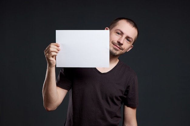 Mężczyzna trzyma pusty arkusz papieru plakat w jego ręce. Uśmiech i radość, miejsce na tekst, miejsce