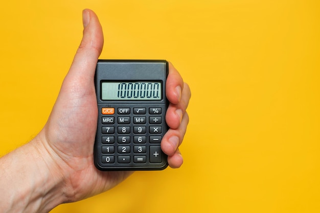 Mężczyzna trzyma w dłoni kalkulator na żółtym tle Pojęcie wysokiej wydajności ceny