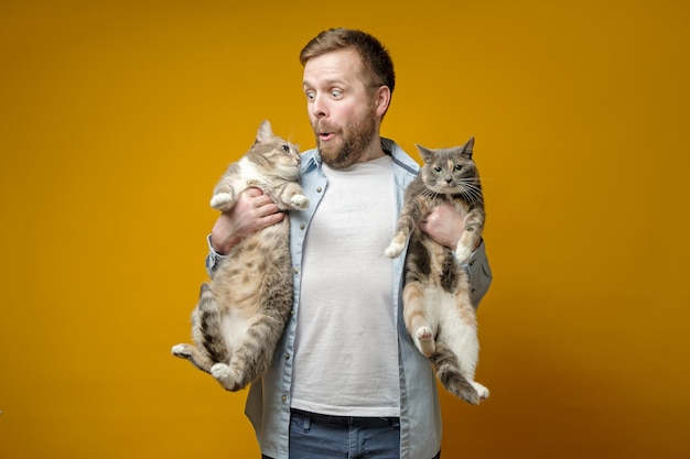 mężczyzna trzyma w rękach dwa ze swoich uroczych kotów, patrzy na jednego z nich i robi zabawny grymas