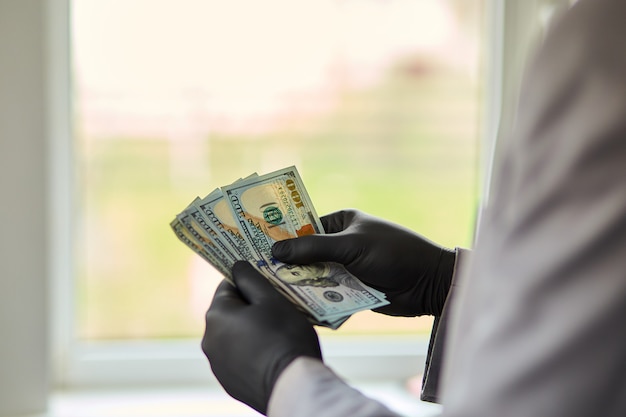 Mężczyzna trzyma w ręku pieniędzy dolarów w czarne rękawiczki medyczne.