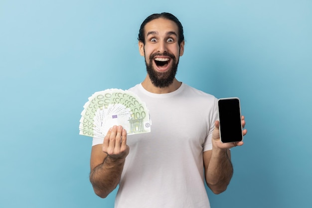 Mężczyzna trzymający banknoty euro i telefon komórkowy z pustym wyświetlaczem makiety do reklamy