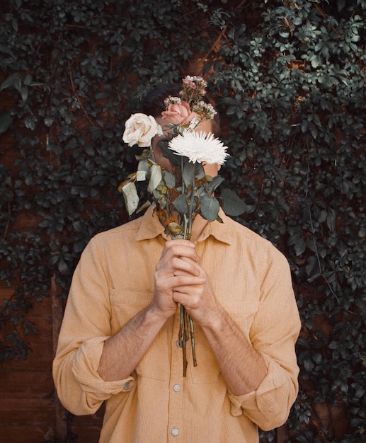 Zdjęcie mężczyzna trzymający kwiaty stojący przeciwko roślinie