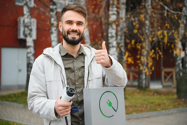 Mężczyzna trzymający ładowarkę do samochodów elektrycznych na stacji ładującej