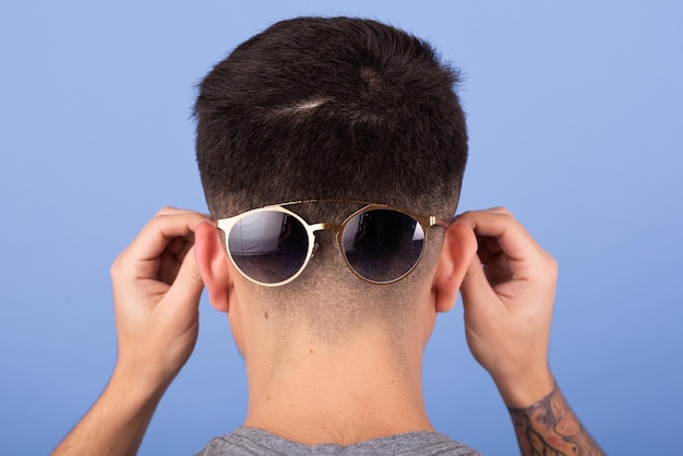 mężczyzna trzymający okulary przeciwsłoneczne z tyłu głowy dwiema rękami, na niebieskim tle