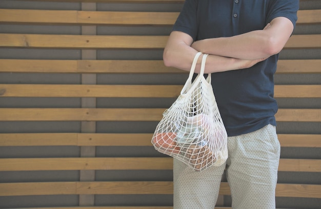 mężczyzna trzymający siatkową torbę z produktami bez plastikowego opakowania