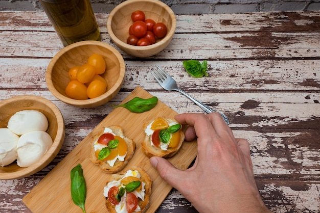 Zdjęcie mężczyzna trzymający smaczną bruschettę z mozzarellą, pomidorem, bazylią i olejem składniki na tle