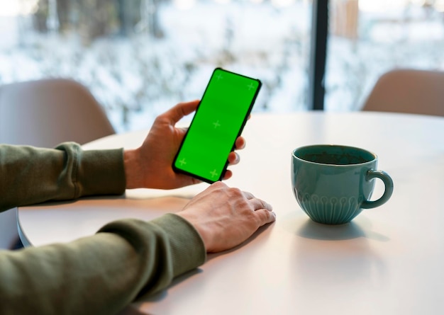 Mężczyzna trzymający smartfon z ekranem Chroma Key pijący kawę z zielonym ekranem biznes makieta