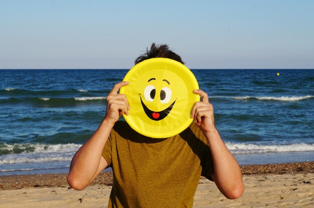 Zdjęcie mężczyzna trzymający talerz przed twarzą, stojąc na plaży