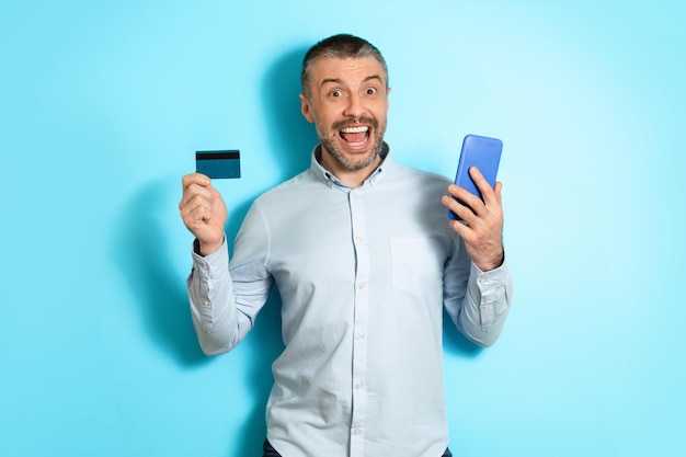 Mężczyzna trzymający telefon komórkowy i kartę kredytową robiący zakupy online na niebieskim tle