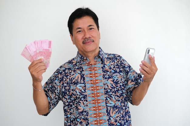 Mężczyzna trzymający telefon komórkowy i pieniądze w gotówce uśmiecha się radośnie