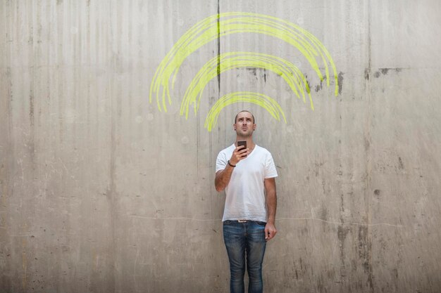 Mężczyzna trzymający telefon komórkowy z żółtym kredowym znakiem wifi nad głową