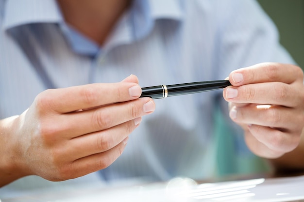 Mężczyzna trzymający w obu ramionach czarny długopis w geście myślenia podczas spotkania lub negocjacji