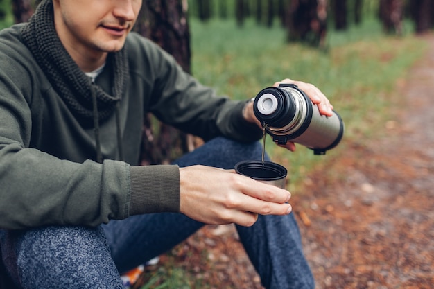Mężczyzna turysta nalewa gorącą herbatę z termosu w wiosennym lesie. Koncepcja kempingu, podróży i sportu