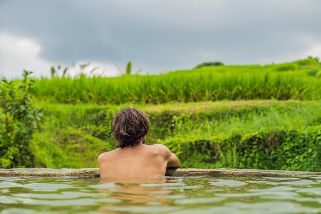 Mężczyzna turysta w gorących źródłach Belulang na Bali na tle tarasów ryżowych.