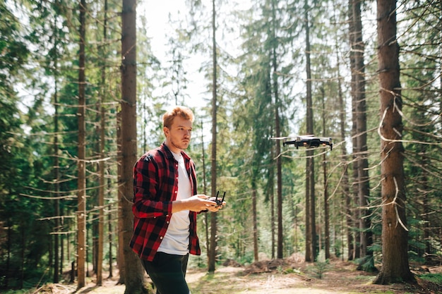 Mężczyzna turysta z pilotem w rękach leci dronem przez gęsty letni las z poważną miną