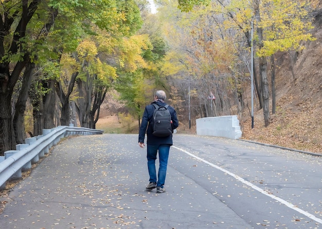 Mężczyzna turysta z plecakiem wspina się drogą pod górę w jesienny dzień