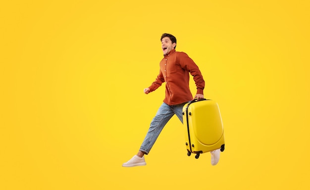 Mężczyzna turysta z walizką biegnącą w żółtym tle w powietrzu