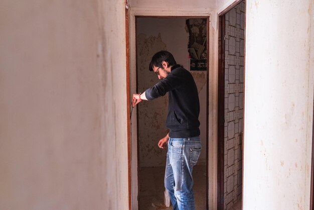 Zdjęcie mężczyzna usuwa tapetę ze ściany korytarza za pomocą skrobaka. pracuje w domu