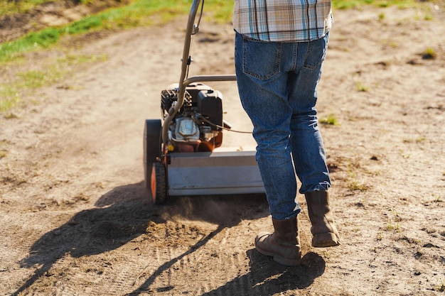 Mężczyzna używający napowietrzacza do wertykulacji i napowietrzania trawnika lub łąki