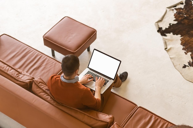 Mężczyzna używający notebooka z pustym ekranem w salonie.