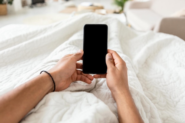 Mężczyzna używający telefonu komórkowego z pustym ekranem w sypialni pov
