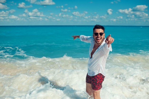 Mężczyzna w białej koszuli wskazujący na morze i uśmiechający się do przodu na niebiesko