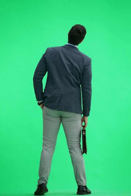 Mężczyzna w biurowej odzieży z walizką na zielonym tle czeka na coś z tyłu