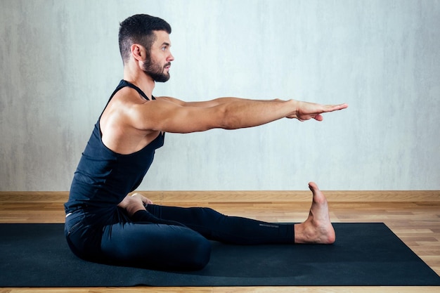 Mężczyzna w ciemnej odzieży sportowej uprawiania jogi na ciemnym tle. asana na podłodze na matach do jogi. pojęcie koncentracji i posiadania ciała