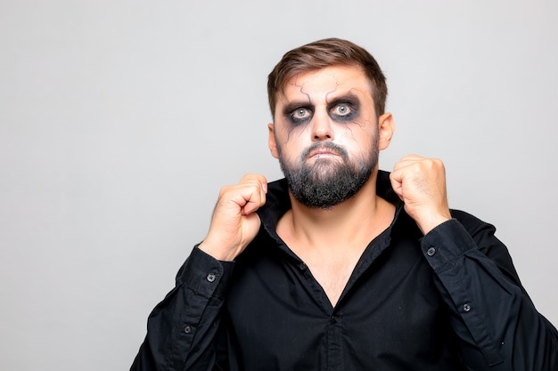 Mężczyzna w czarnej koszuli stoi na białym tle i ma makijaż w stylu nieumarłych na Halloween