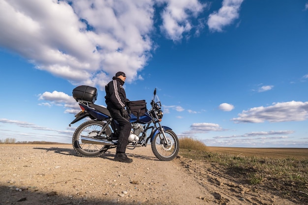 Mężczyzna w czarnym mundurze na rowerze na tle panoramy pola i koncepcji podróży motocyklem błękitnego nieba