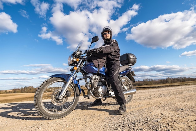 Mężczyzna w czarnym mundurze na rowerze na tle panoramy pola i koncepcji podróży motocyklem błękitnego nieba