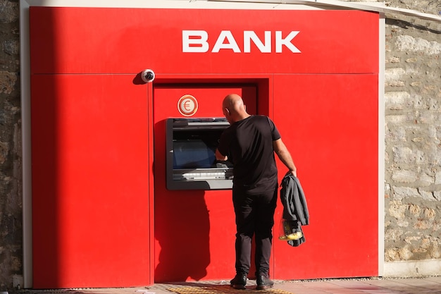 Mężczyzna w czerni wypłaca pieniądze i korzysta z bankomatu euro na ulicy
