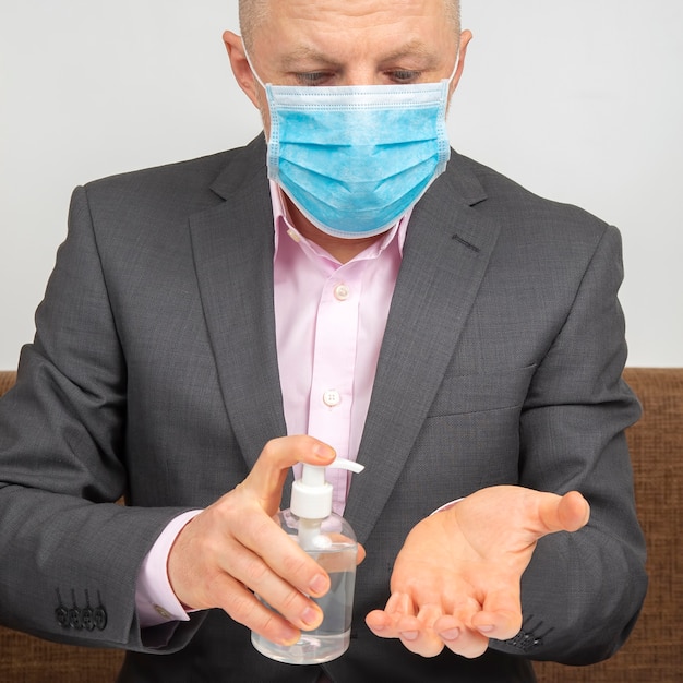 Mężczyzna w domu poddany kwarantannie z maską medyczną na twarzy dezynfekuje ręce roztworem alkoholu z infekcji wirusem