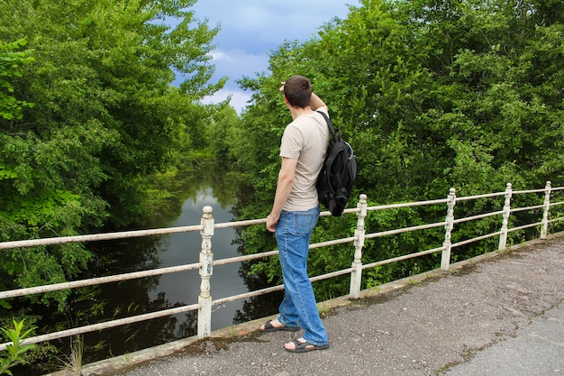 Mężczyzna W Dżinsach I Plecaku Na Moście Patrzący W Dal Na Drzewa