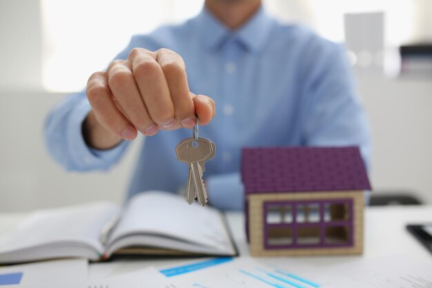 Mężczyzna w garniturze daje klucz do odblokowania nowego miniaturowego domu kup nowe mieszkanie