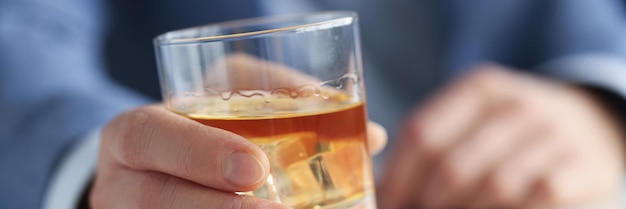 Mężczyzna w garniturze trzymający szklankę whisky z lodem w dłoni zbliżenie leczenie uzależnienia od alkoholu