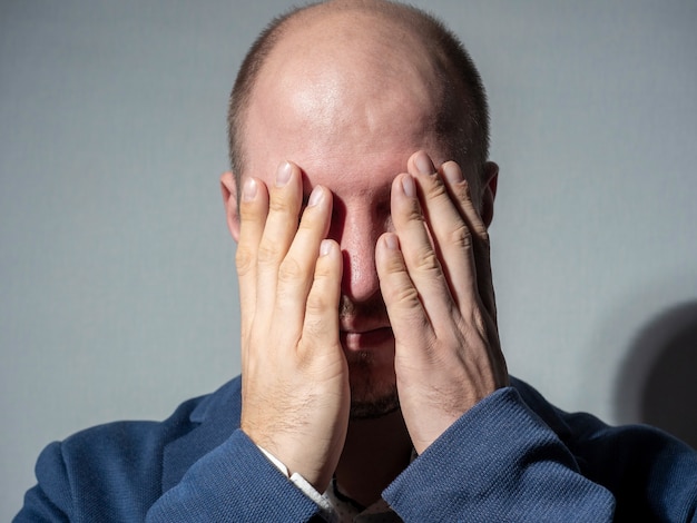 Mężczyzna w garniturze zakrył oczy dłońmi. Portret z bliska. Przestraszony, kłapiący, przymykający oko na to, co się dzieje. Emocja