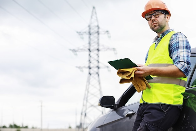 Mężczyzna w hełmie i mundurze, elektryk w terenie. Zawodowy inżynier elektryk sprawdza linie energetyczne podczas pracy.