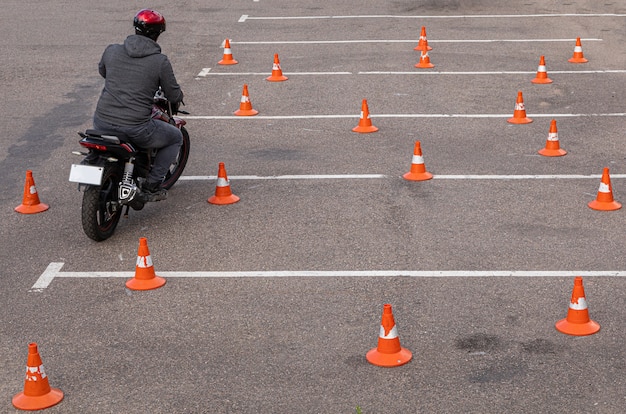 Mężczyzna W Hełmie Na Motocyklu Robi ćwiczeniom Na Parkingu Wśród Pomarańczowych Szyszek Ruchu