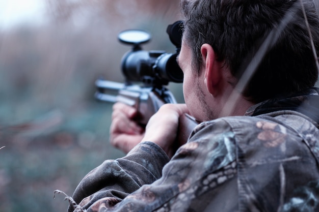 Zdjęcie mężczyzna w kamuflażu z karabinem myśliwskim w lesie na wiosennym polowaniu