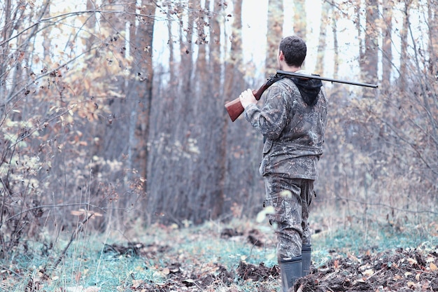 Mężczyzna w kamuflażu z karabinem myśliwskim w lesie na wiosennym polowaniu