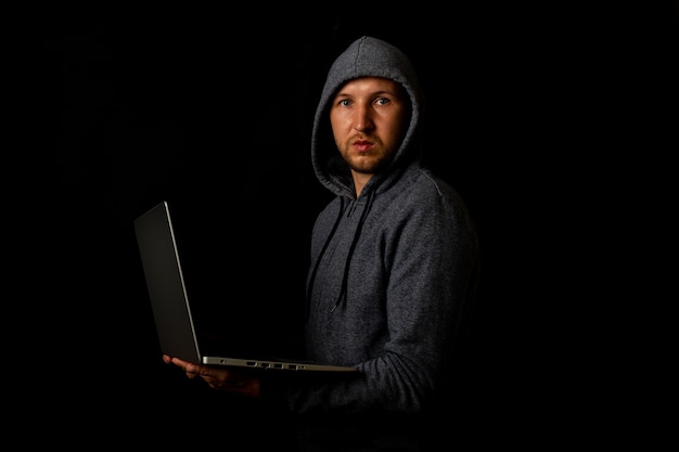 Mężczyzna w kapturze trzyma laptopa w rękach w ciemności