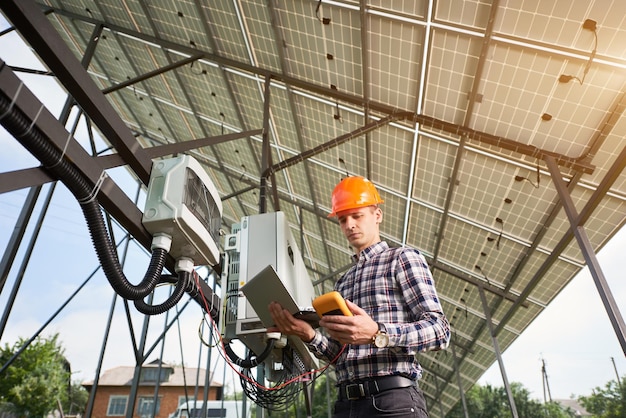 Mężczyzna W Kasku Stojący Z Laptopem W Pobliżu Sprzętu Elektrycznego W Elektrowni Słonecznej