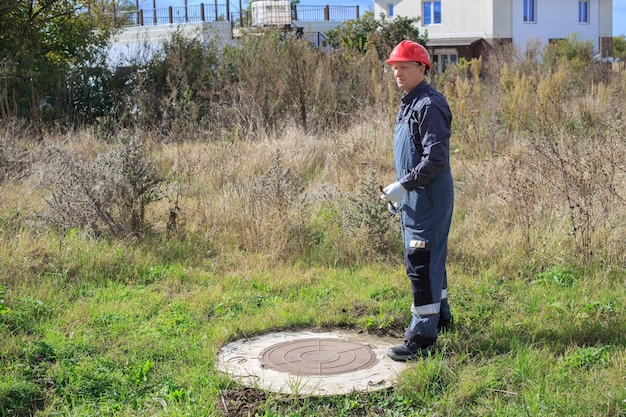 Mężczyzna w kombinezonie i kasku przy studni na wsi Inspekcja studni i liczników