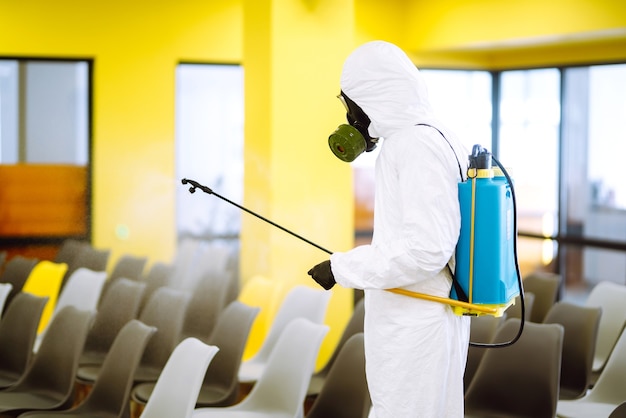 Mężczyzna w kombinezonie ochronnym dezynfekuje halę montażową za pomocą chemikaliów w sprayu, aby zapobiec koronawirusowi.