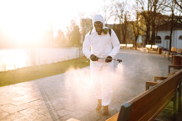 Mężczyzna w kombinezonie ochronnym i masce antywirusowej dezynfekuje miejsca publiczne środkami chemicznymi w sprayu Covid19